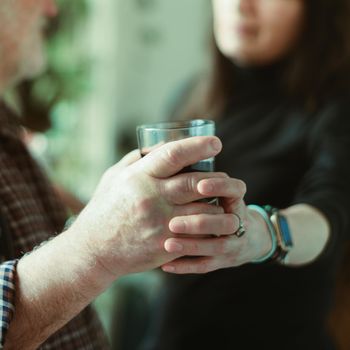 caucasian man drinking red wine and getting drunk at home stressing younger hispanic womancaregiver adn wife - alcoholism and domestic violence concept. High quality photo