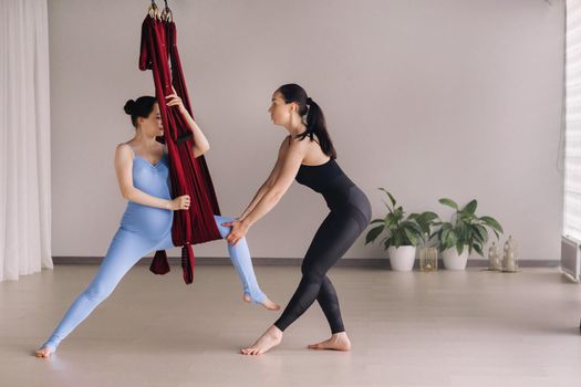 Pregnant girl. A woman with a trainer does yoga in a hammock in the gym. The concept of a healthy lifestyle, motherhood.