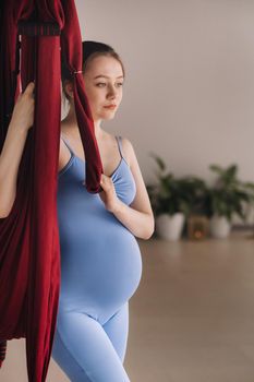 Pregnant girl. A woman in sportswear stands near a hanging hammock in the gym. The concept of a healthy lifestyle, motherhood.