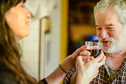 caucasian man drinking red wine and getting drunk at home stressing younger hispanic womancaregiver adn wife - alcoholism and domestic violence concept. High quality photo