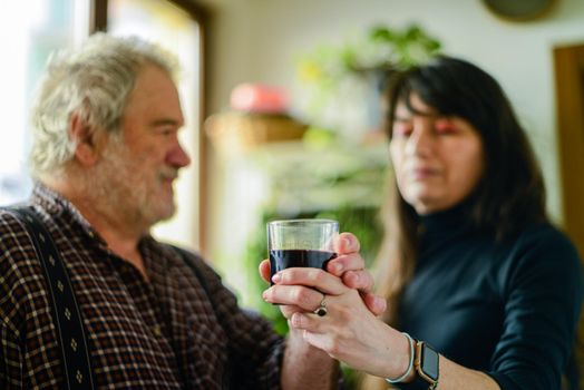 caucasian man drinking red wine and getting drunk at home stressing younger hispanic womancaregiver adn wife - alcoholism and domestic violence concept. High quality photo