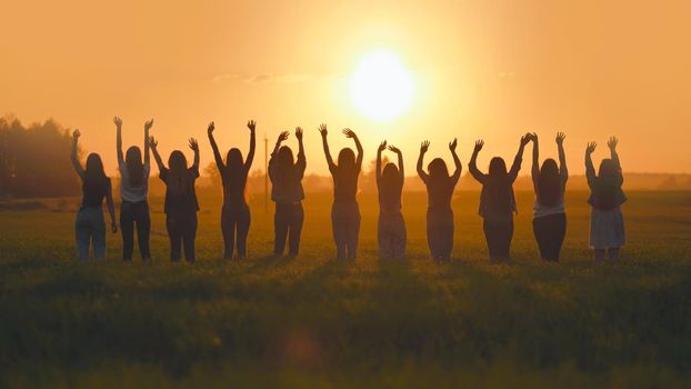 Silhouette of friends of 11 girls waving their hands at sunset in the field