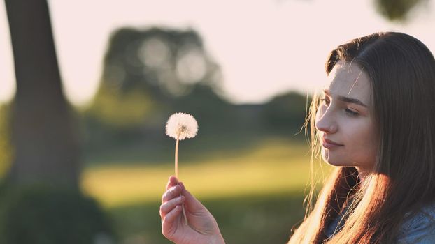 A young girl gently looks at the dandelion flower