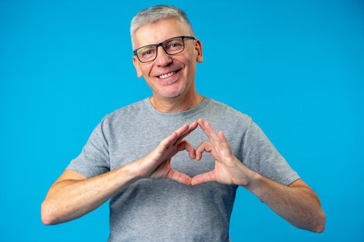 Middle age handsome man showing heart symbol on blue background, close up