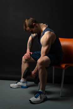 Man on black background keeps sits on a chair rocking his biceps dumbbells pumped up in fitness bodybuilding sexy sport, athlete weight strong athletic hand, person lifestyle. Young skin power, human fit