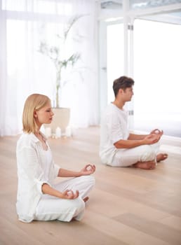 Two people sitting in the lotus position in a yoga studio.