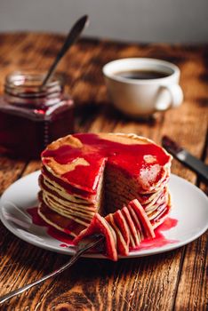 Stack of pancakes with berry jam on white plate over wooden table
