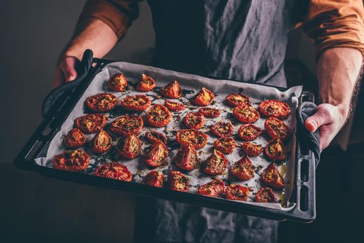 Baking Sheet Full of Freshly Oven Baked Tomatoes with Olive Oil and Thyme in a Male Hands