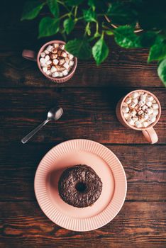 Stack of Homemade Chocolate Donuts and Mugs of Hot Chocolate with Marshmallow on Rustic Wooden Surface. View from Above