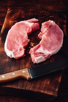 Two pork loin steaks with knife on rustic cutting board