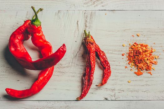 Fresh, dried and crushed red chili pepper over colored wooden background