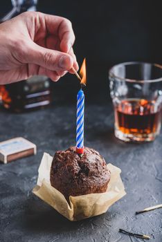 Hand lighting candle with a match on birthday chocolate muffin