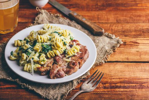 Pork Neck Steak with Creamy Spinach Pasta Garnished with Grated Parmesan Cheese on White Plate