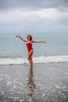 A beautiful and sexy brunette in a red swimsuit on a pebble beach, Running along the shore in the foam of the waves.