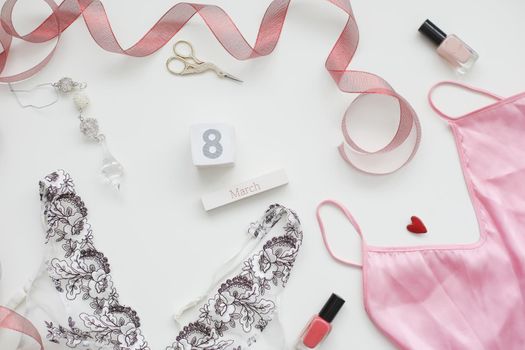 Flat lay composition of female underwear with a red ribbon and cosmetics on white background. Styled flat lay, top view, copy space. Concept Women's Day, March 8. 