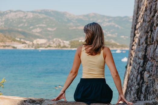 Beautiful girl sitting on a stone wall, in background is the blue sea, Budva, Montenegro