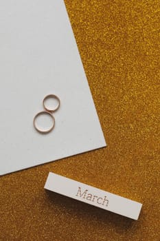 8 March, International Women's Day background with decor elements. Eight made of two gold wedding rings and word MARCH. Greeting card for March 8. Flat lay, top view, copy space