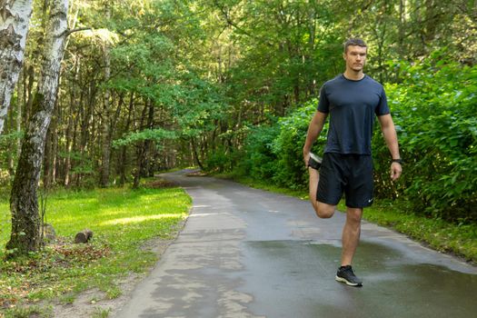 A man athlete runs in the park outdoors, around the forest, oak trees green grass young enduring athletic athlete sport jogger young jog, jogging outside. Adult runners stretches