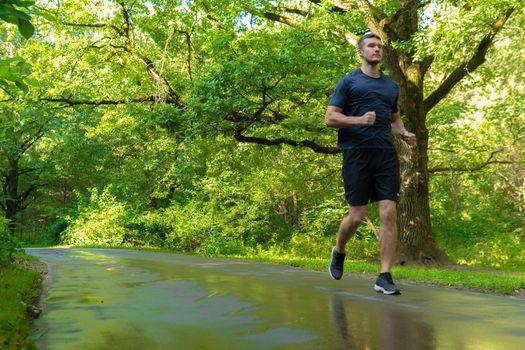 A man athlete runs in the park outdoors, around the forest, oak trees green grass young enduring athletic athlete run sport nature, fitness outdoor wellbeing. leisure feet stretches