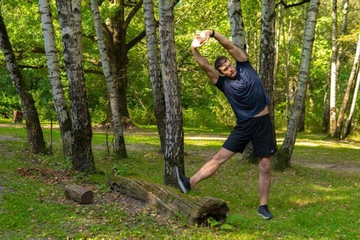 A young enduring athletic athlete is doing stretching in the forest outdoors, around the forest, oak trees.healthy exercise, lifestyle athletic recreation marathon, man. Summer leisure running, morning stretches