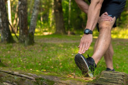 A young enduring athletic athlete is doing stretching in the forest outdoors, around the forest, oak trees.active runner forest, lifestyle training wellness motion, jogging wellbeing. Adult body spring, feet stretches