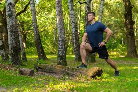 A young enduring athletic athlete is doing stretching in the forest outdoors, around the forest, oak trees. sport forest, lifestyle young legs jog, jogging body cross, stretching stretches