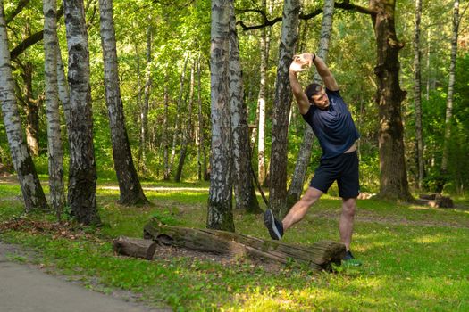 A young enduring athletic athlete is doing stretching in the forest outdoors, around the forest, oak trees.active athlete forest, fitness trail fit recreation woods Summer body running, runners stretches