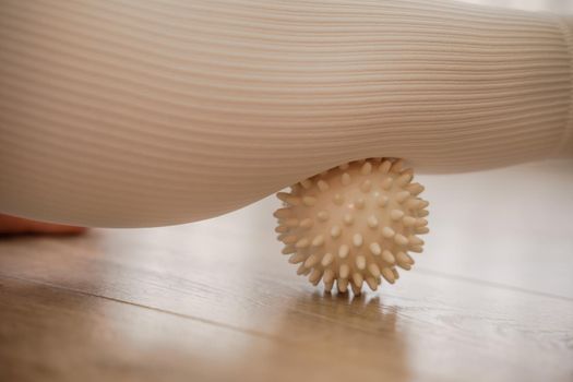 Athletic slim caucasian woman doing thigh self-massage with a massage ball indoors. Self-isolating massage.