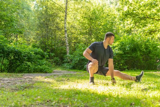 A young enduring athletic athlete is doing stretching in the forest outdoors, around the forest, oak trees.healthy runner forest, trail person motion, park wellbeing. Adult cross, feet stretches