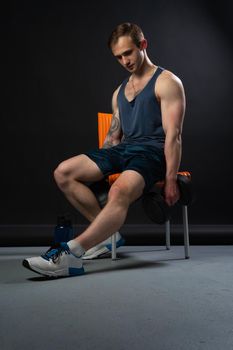 Man on black background keeps dumbbells pumped up in fitness bodybuilding chest torso, arm weight strong healthy Young guy fit sitting on a chair resting after a workout