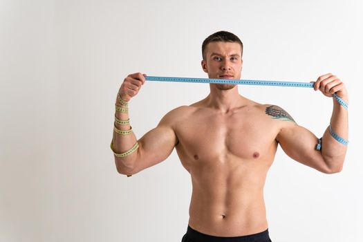 A man measures the waist of a metre and poses against a white background isolated young muscular bodybuilder Measure beautiful caucasian sport attractive tape