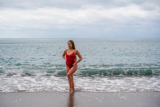 A beautiful and sexy brunette in a red swimsuit on a pebble beach, Running along the shore in the foam of the waves.