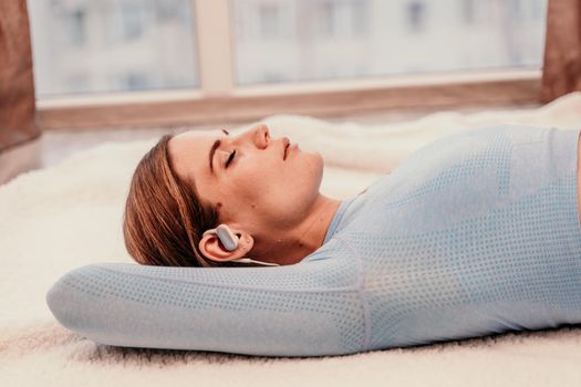 Side view portrait of relaxed woman listening to music with headphones lying on carpet at home. She is dressed in a blue tracksuit