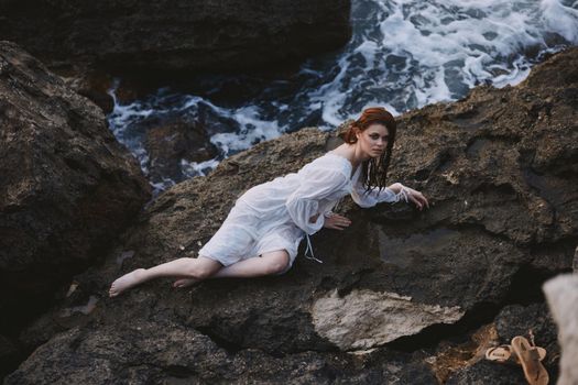 beautiful young woman in long white dress wet hair lying on a rocky cliff unaltered. High quality photo