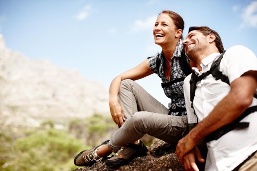 Two hikers laughing and smiling while enjoying a mountain top view.