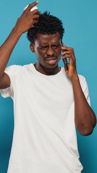 Black person using smartphone for phone call in studio. African american man answering call and feeling worried about news. Frustrated adult using phone for remote communication