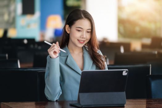 A female entrepreneur or businesswoman showing a smiling face while operating a computer tablet working on a wooden table