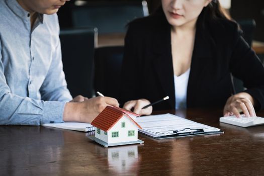 Concept of signing loan agreements, refinancing, buying and selling houses and land, focusing on model houses. A real estate agent is pointing to contract documents for male clients to Buy a dwelling