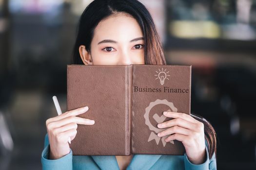 Asia woman entrepreneur or businesswoman showing a smiling face while reading a book developing financial and investing strategies