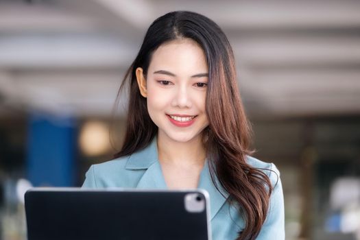 A female entrepreneur or businesswoman showing a smiling face while operating a computer tablet working on a wooden table