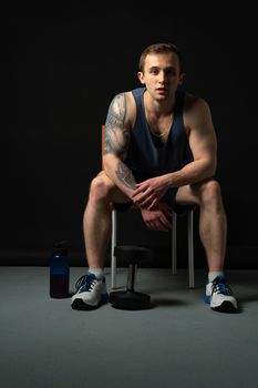 Man on black background keeps dumbbells pumped up in fitness biceps body weight exercise athletic heavy, healthy lifestyle. Lift handsome one fit sitting on a chair resting after a workout