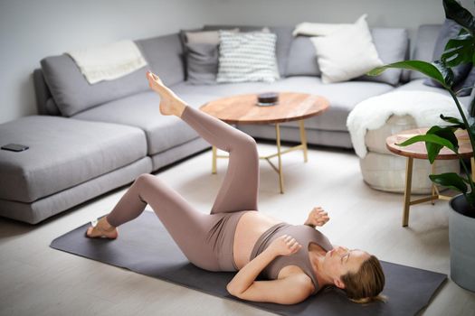Young beautiful pregnant woman training pilates at home in her living room. Healthy lifestyle and active pregnancy and motherhood concept