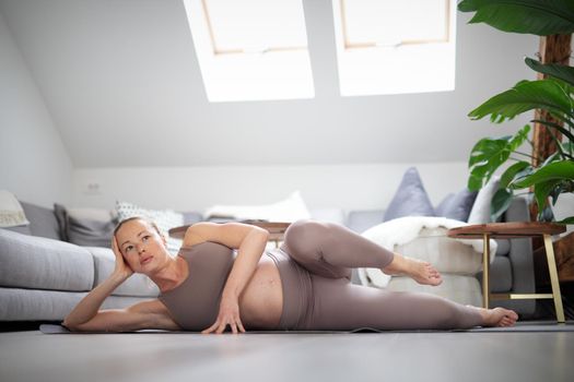 Young beautiful pregnant woman training pilates at home in her living room. Healthy lifestyle and active pregnancy and motherhood concept