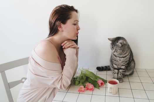 happy woman and her cat smelling fresh pink tulips in the morning at home