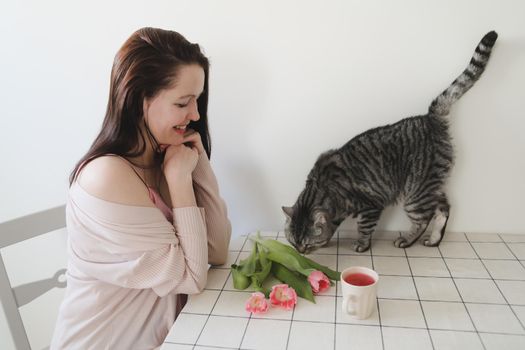 happy woman and her cat smelling fresh pink tulips in the morning at home