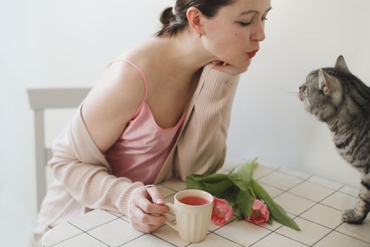 happy woman and her cat smelling fresh pink tulips in the morning at home