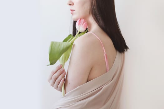 spring portrait of a young woman with pink fresh tulip on white background with copyspace.