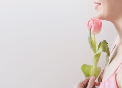 spring portrait of a young woman with pink fresh tulip on white background with copyspace.