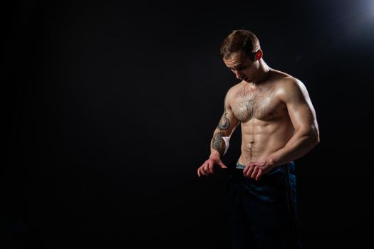 Man on black background keeps dumbbells pumped up in fitness active sport, body muscular strong bodybuilder shirtless lifestyle. Young one fit Look at the press and measures the size of pants for weight loss