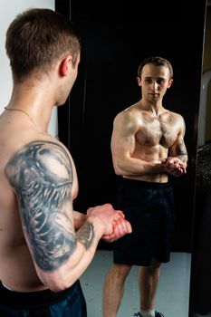 Man on black background keeps dumbbells pumped up in fitness torso, training lifting healthy weightlifting. Attractive handsome adult, gym fit In mirror reflection, the body is pumped up